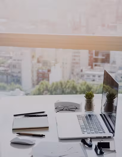 Bureau lumineux avec ordinateur portable, carnet, lunettes et plante, symbolisant un hébergement web fiable et organisé