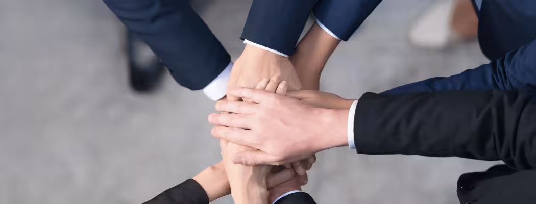 Mains empilées de plusieurs personnes en costume, illustrant l’engagement et l’intégrité de l’équipe Keiyo