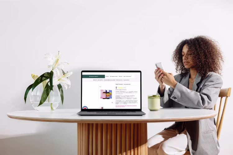 Une femme est assis à un table avec un ordinateur qui affiche une page produit d'Ananda pro