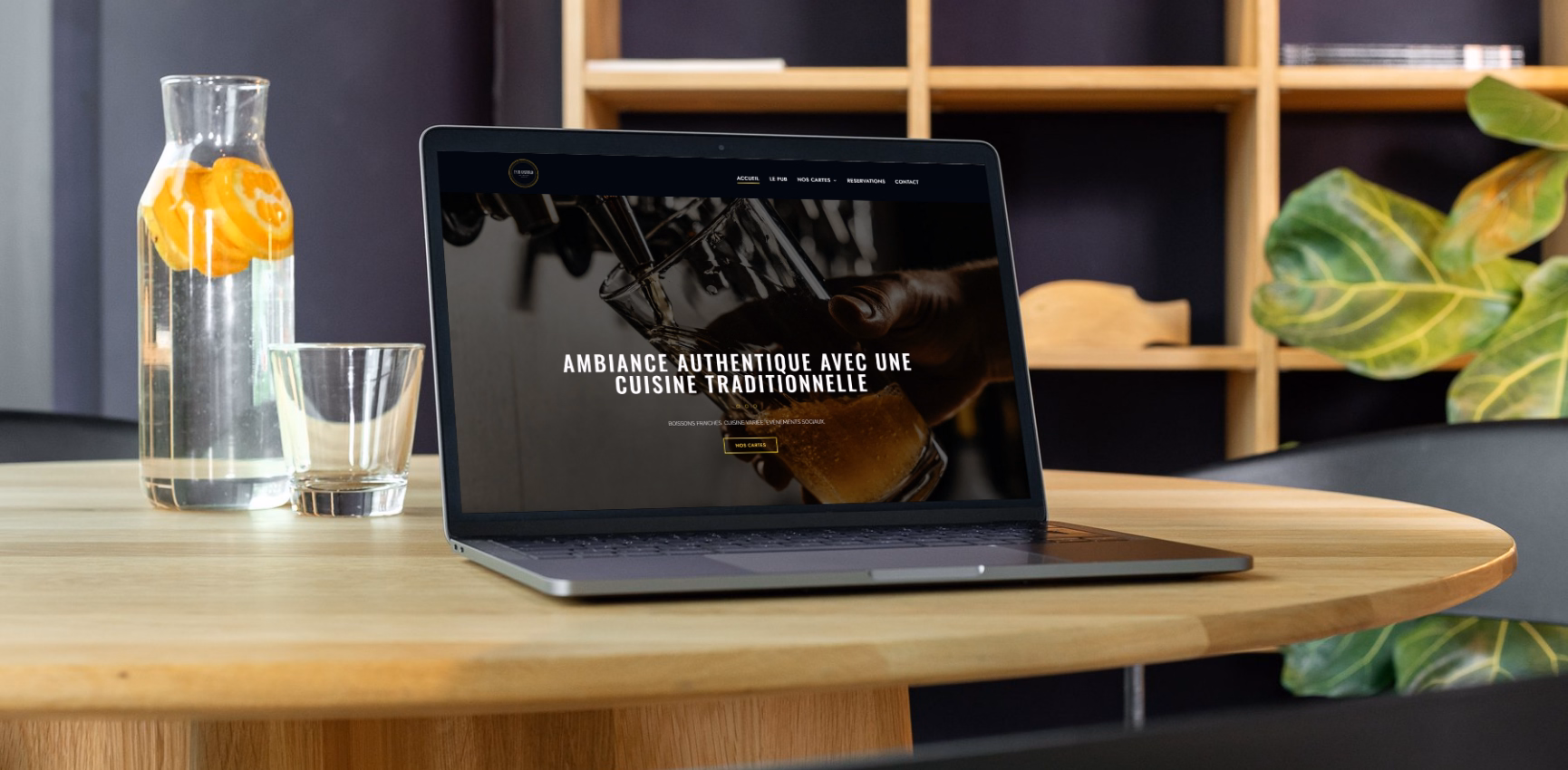 Site vitrine du pub Oxford affiché sur un MacBook posé sur une table en bois dans un cadre chaleureux
